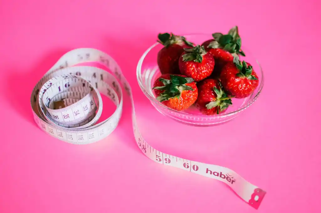 fondo rosa con cinta metrica junto a fresas